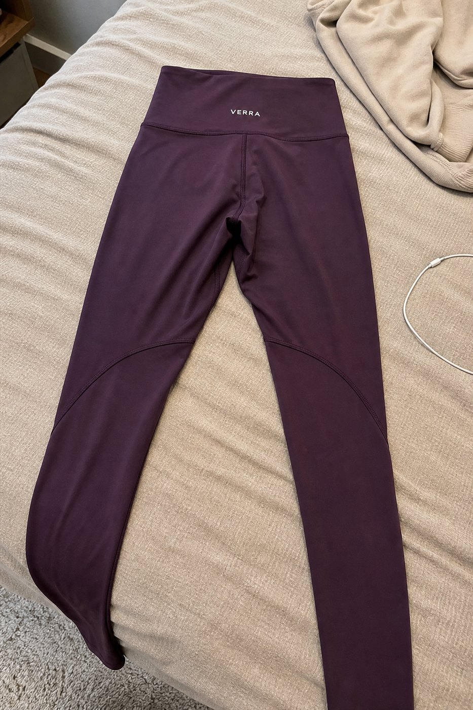 Plum leggings laid flat on a bed, photographed on a phone with a charger cable in frame